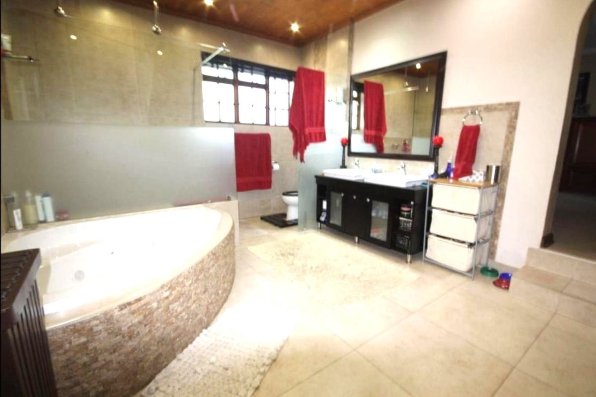 Spacious bathroom featuring a large corner jetted tub, double vanity with integrated sinks, glass-enclosed shower, and tiled flooring.
