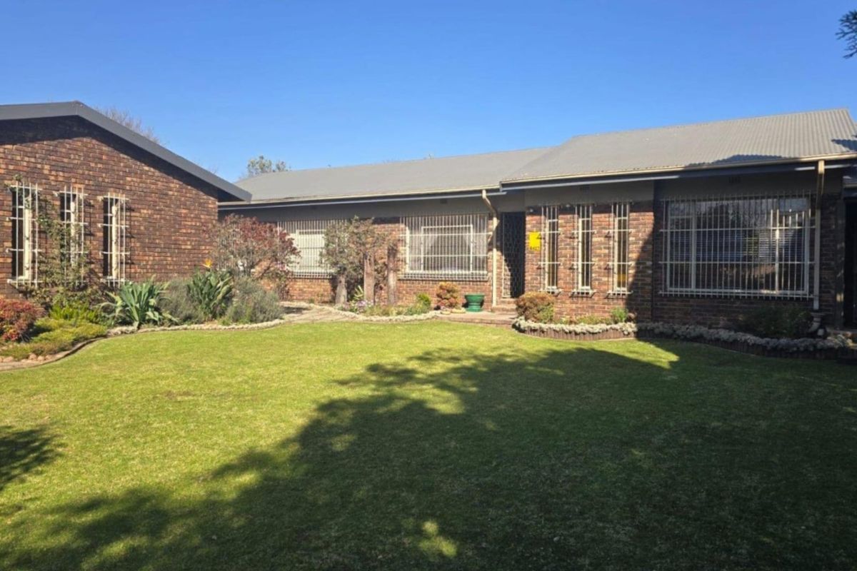 A well-maintained face brick house exterior featuring a spacious lawn, landscaped garden beds, and secure window bars under a corrugated metal roof.