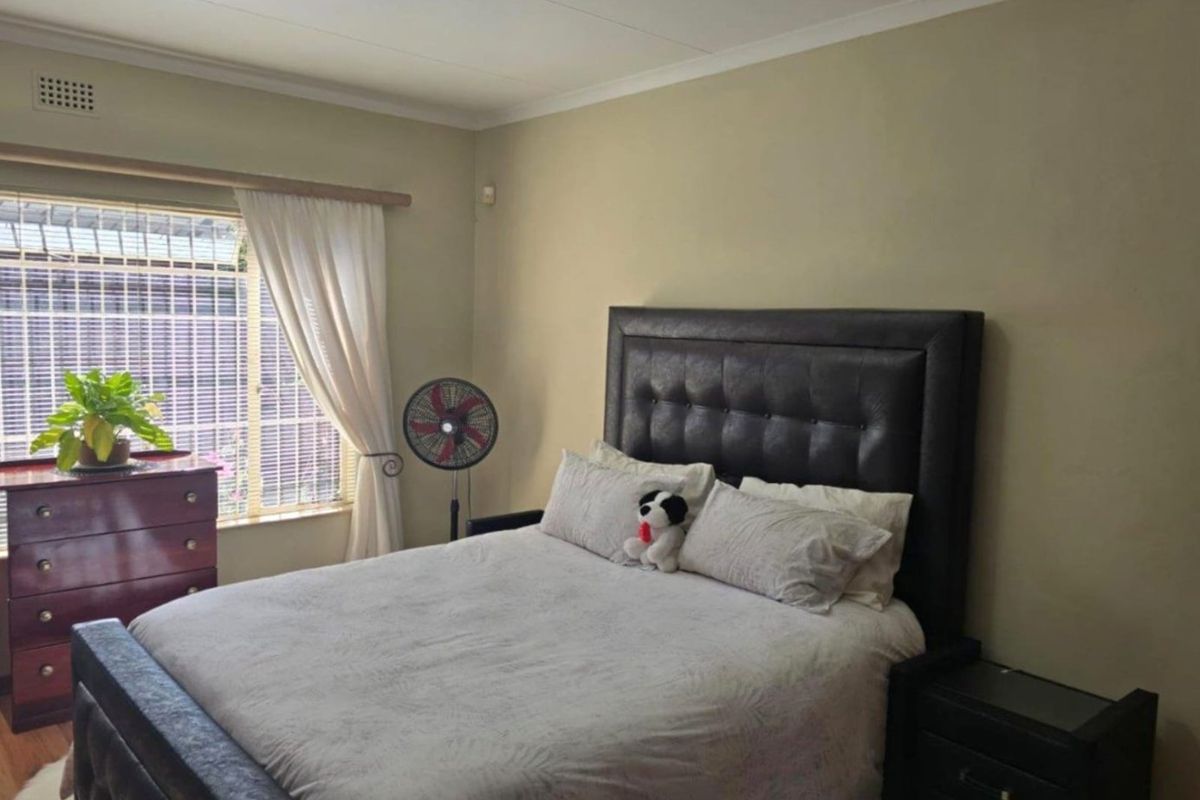 A standard bedroom featuring laminate flooring, neutral wall tones, and a window fitted with security burglar bars.