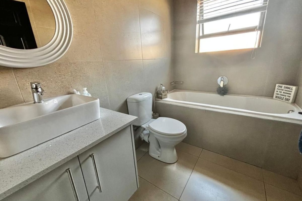 Modern bathroom featuring a vanity with a vessel sink, a built-in bathtub, and a toilet, finished with neutral wall and floor tiles.