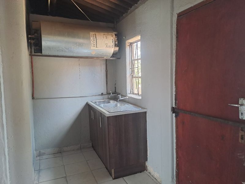 A functional laundry or utility area featuring a stainless steel sink, built-in cabinetry, and an overhead electric water heater.