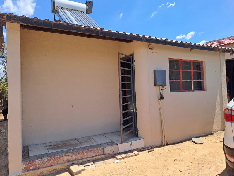 Rear exterior view of the house featuring a small tiled patio, solar water heating system, and security gate access.
