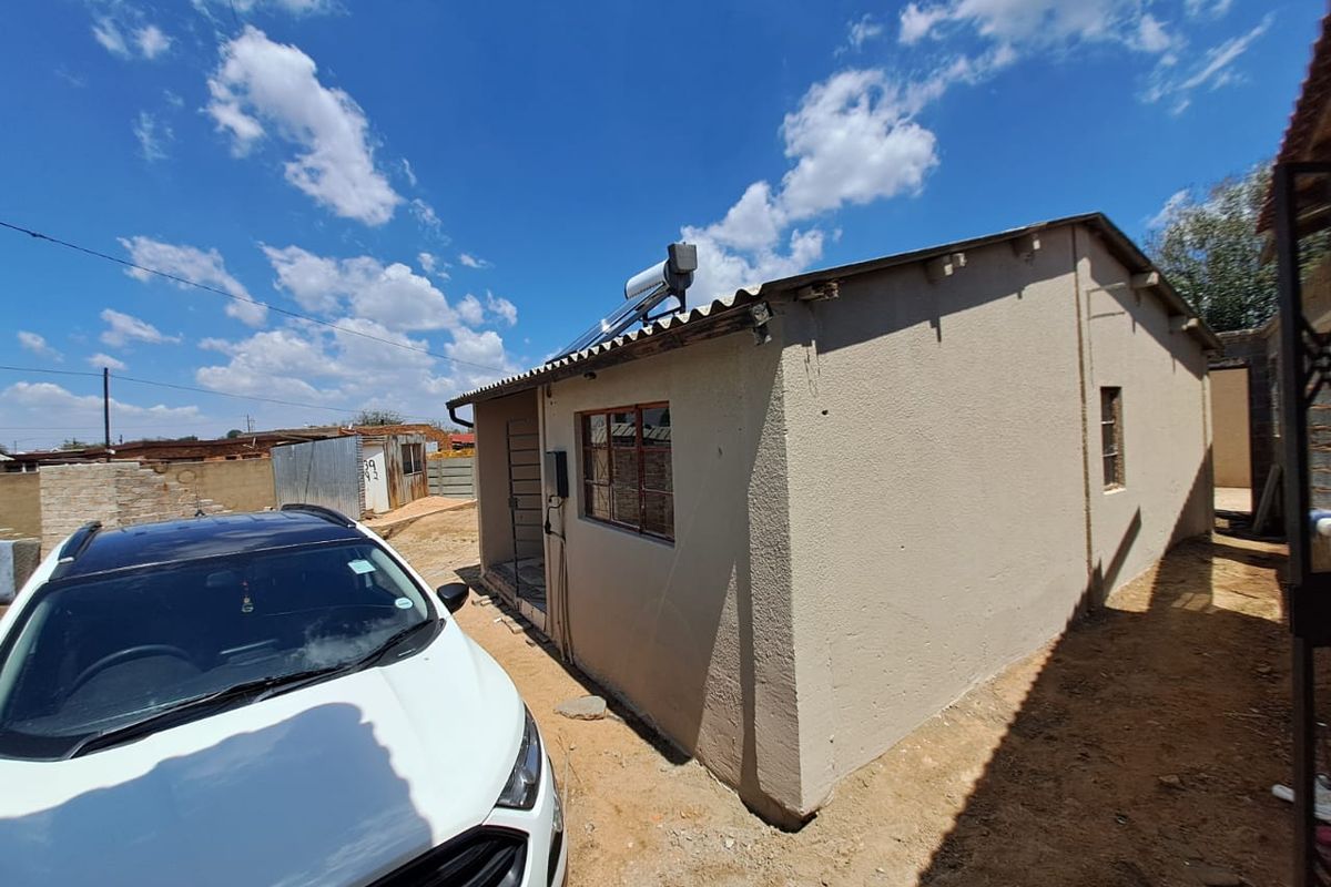 Rear exterior view of the property featuring a solar water heater, plastered walls, and security bars on the windows.