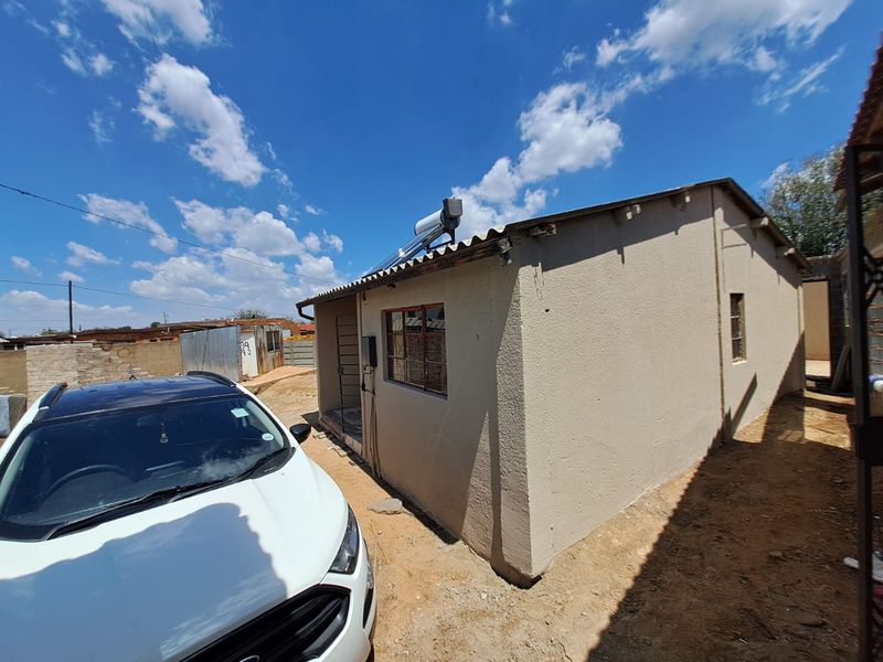 Rear exterior view of the property featuring a solar water heater, plastered walls, and security bars on the windows.