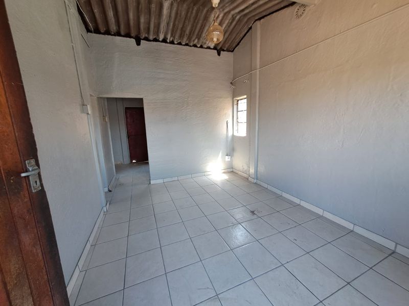An empty bedroom featuring tiled flooring, exposed corrugated ceiling, and a simple timber door, offering a blank canvas for renovation.