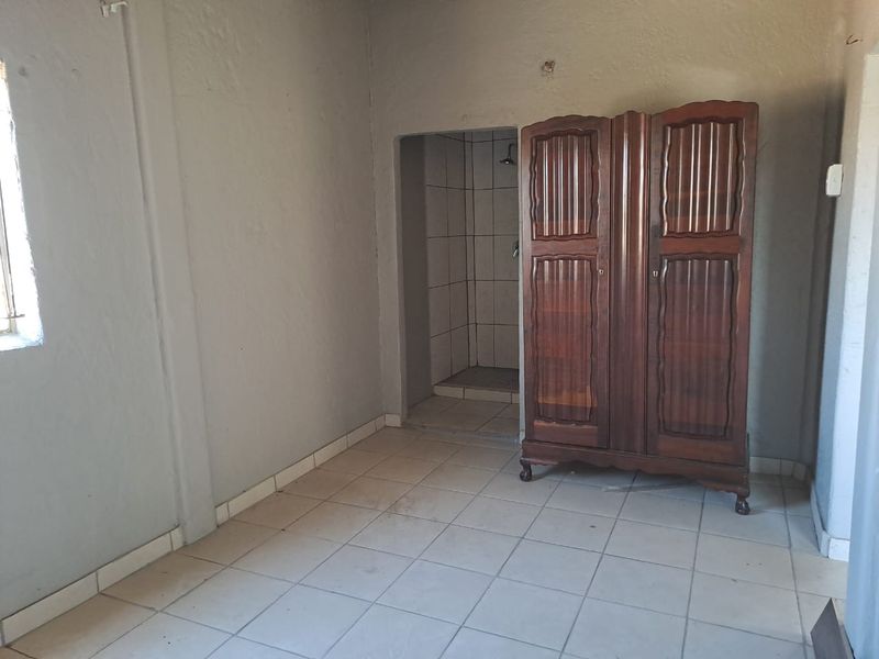 A bedroom featuring tiled flooring and an integrated en-suite shower area, requiring cosmetic updates to improve the overall finish and condition.
