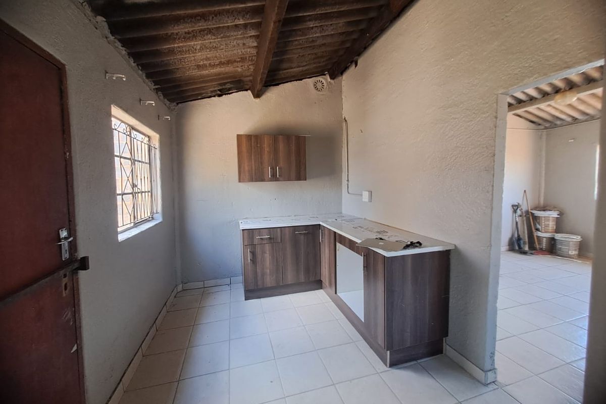 A basic, unfinished kitchen area featuring wood-look cabinetry, tiled floors, and exposed timber roof beams, offering a blank canvas for renovation.