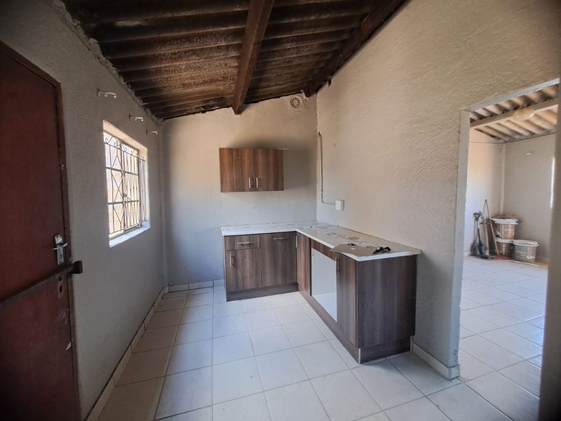 A basic, unfinished kitchen area featuring wood-look cabinetry, tiled floors, and exposed timber roof beams, offering a blank canvas for renovation.