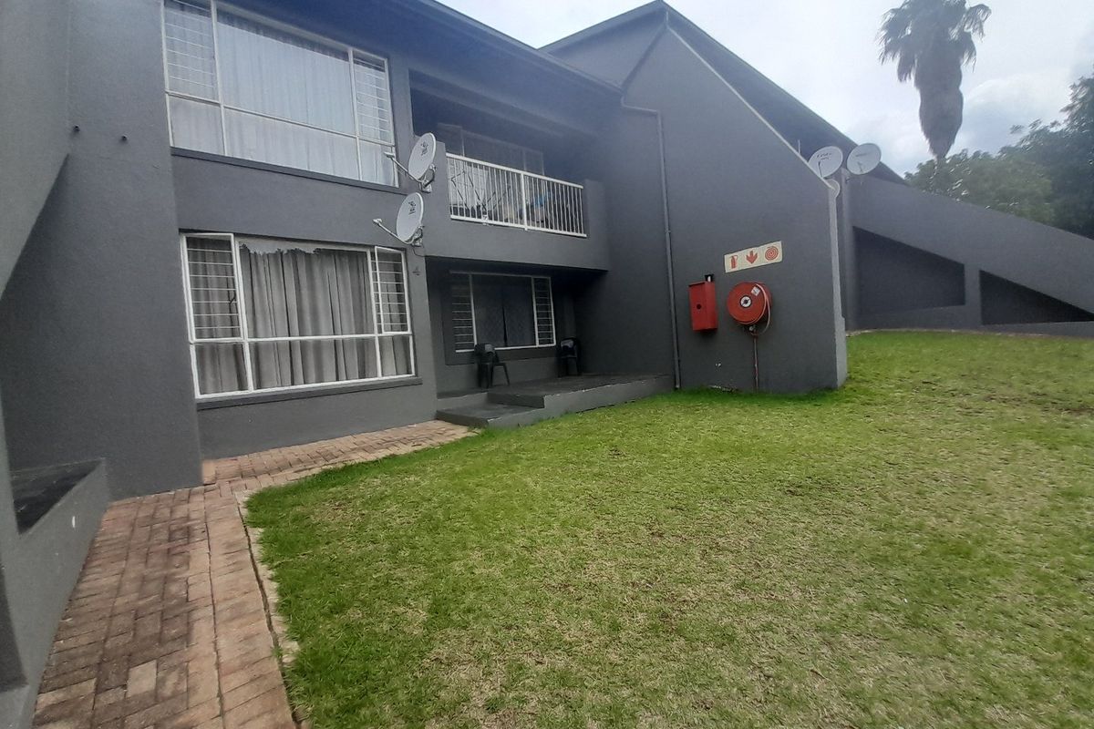 Rear view of the apartment building featuring a lawn, paved walkway, balcony, and essential fire safety equipment mounted on the exterior wall.