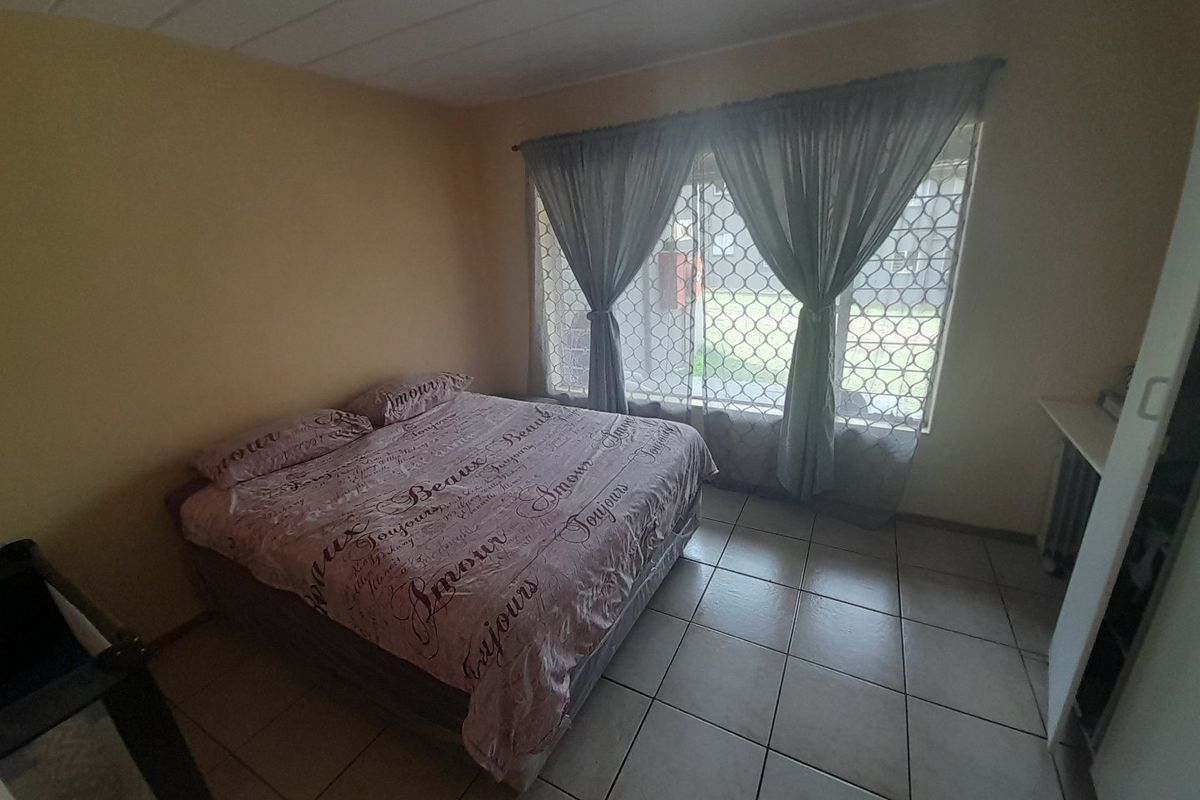 A functional bedroom featuring tiled flooring, a security gate on the window, and built-in cupboard storage.