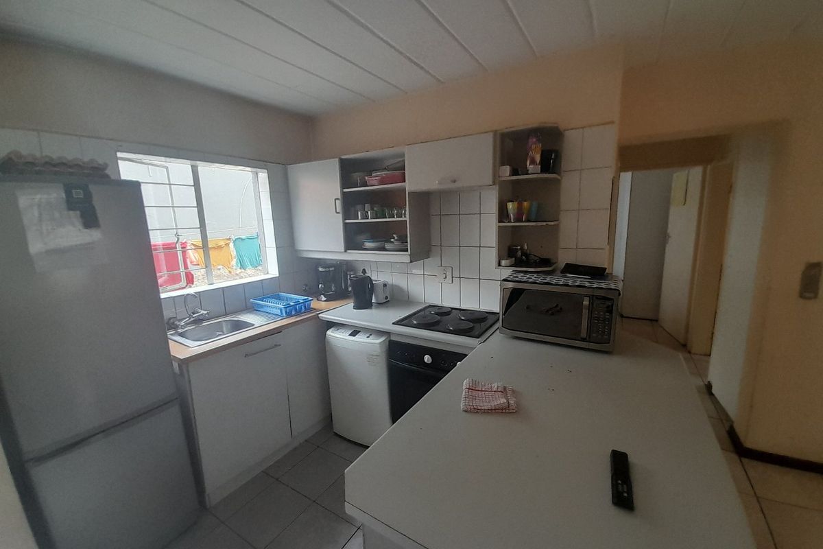 A functional kitchen featuring built-in cabinetry, a stainless steel sink, an electric hob, and an oven, with tiled flooring and backsplash throughout.