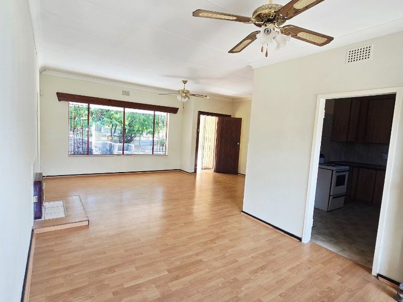 Spacious open-plan living area featuring laminate flooring, ceiling fans, and a fireplace hearth, with direct access to the kitchen.