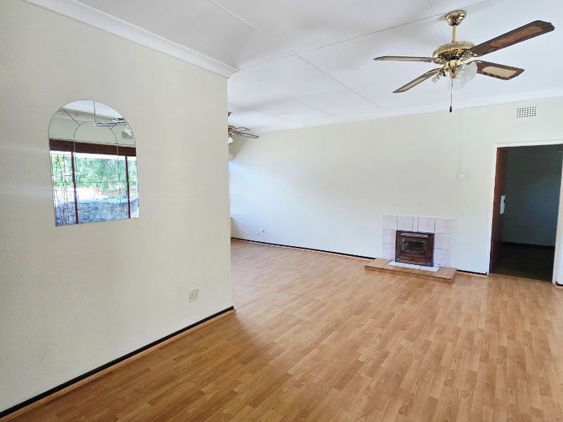 Spacious living area featuring laminate flooring, a built-in fireplace, and a ceiling fan, offering a clean, neutral canvas for interior design.