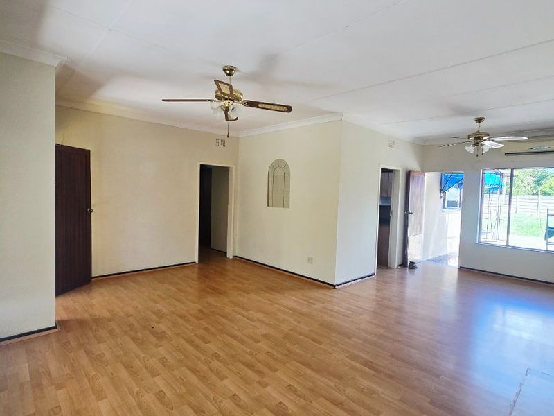 Spacious, empty living area featuring laminate flooring, dual ceiling fans, and natural light through a sliding glass door leading to the exterior.