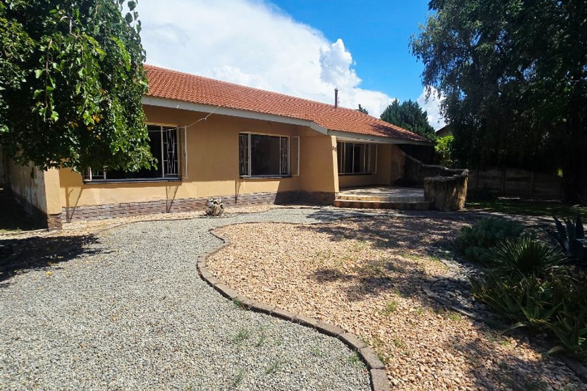 Rear view of the house featuring a tiled roof, stone-clad plinth, and a gravel-landscaped garden with a paved patio area.