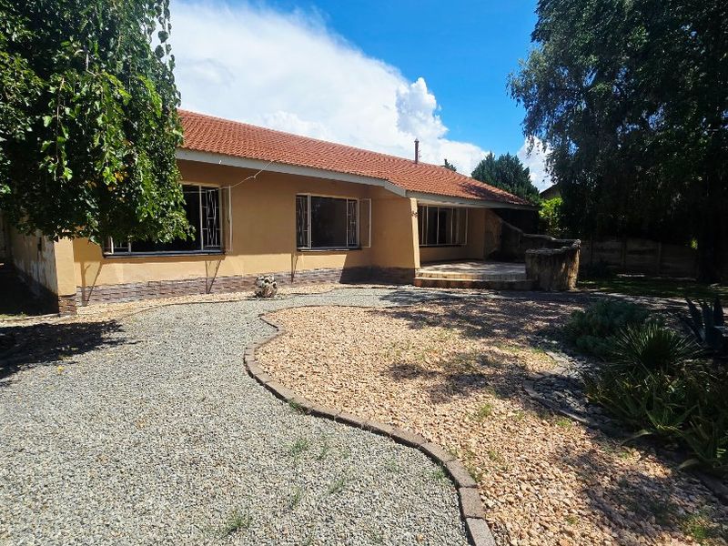 Rear view of the house featuring a tiled roof, stone-clad plinth, and a gravel-landscaped garden with a paved patio area.