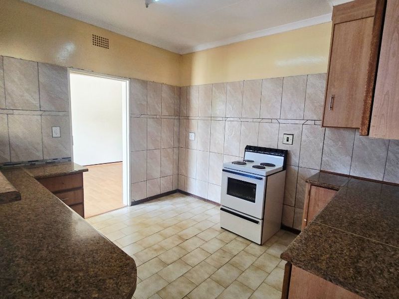A functional kitchen featuring granite countertops, tiled splashbacks, and built-in cabinetry, offering a clean and practical space ready for updates.