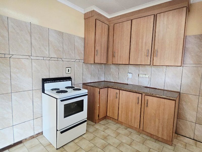 A functional kitchen featuring wood-look cabinetry, laminate countertops, tiled walls, and a freestanding stove, offering a clean space ready for modernization.