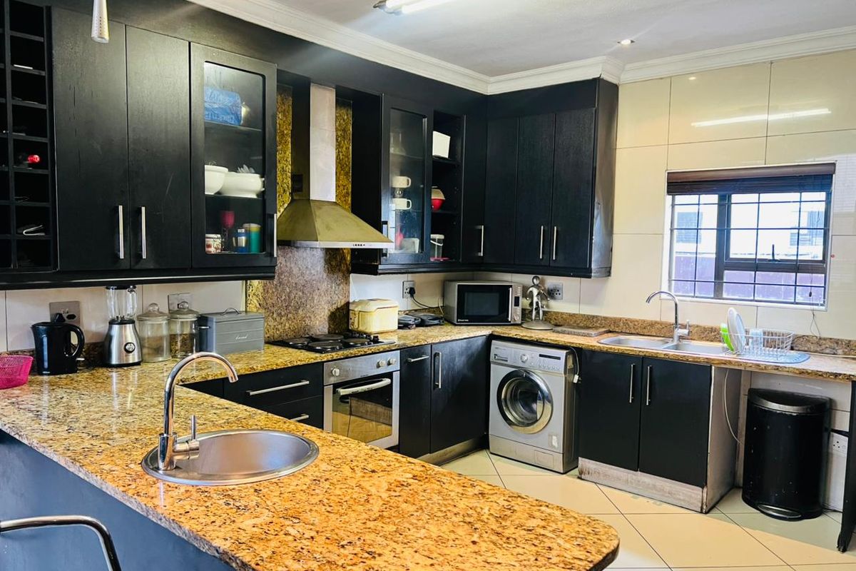 A functional kitchen featuring dark cabinetry, granite countertops, a gas hob, built-in oven, and tiled flooring with a breakfast bar area.