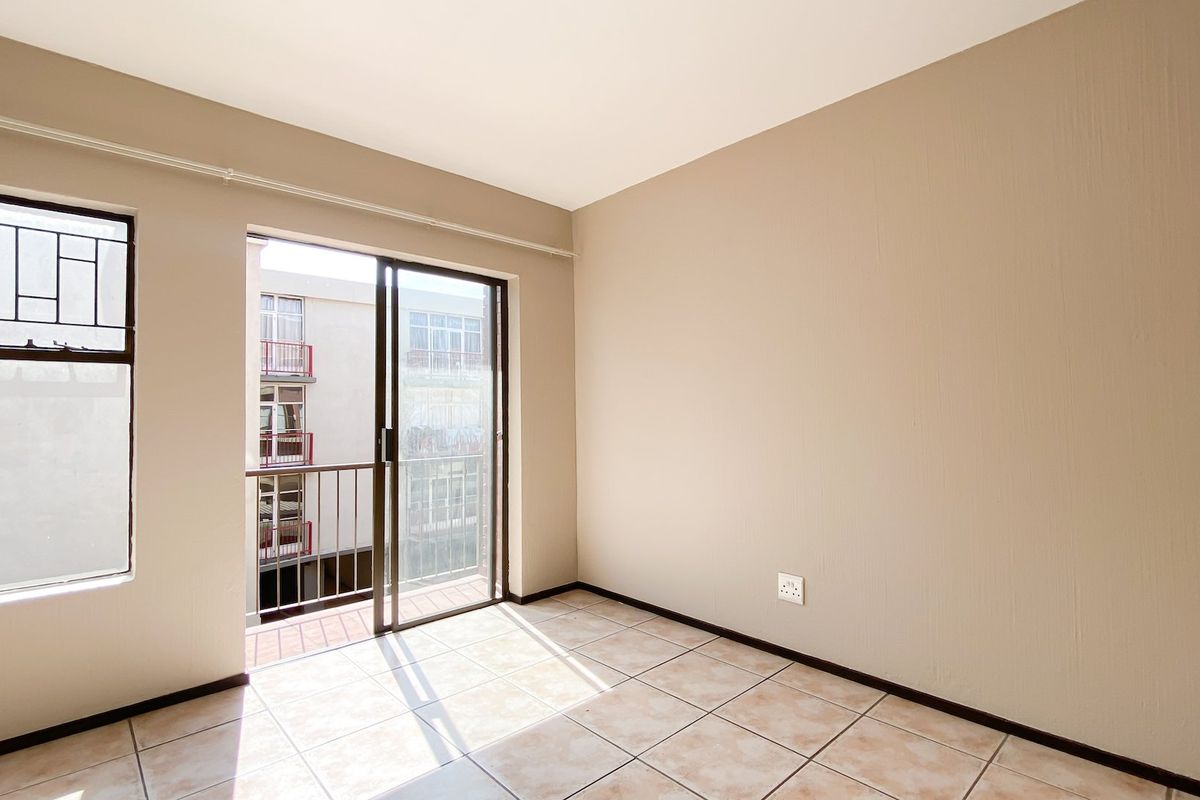 An empty bedroom featuring tiled flooring, neutral walls, and a sliding glass door providing access to a small balcony.