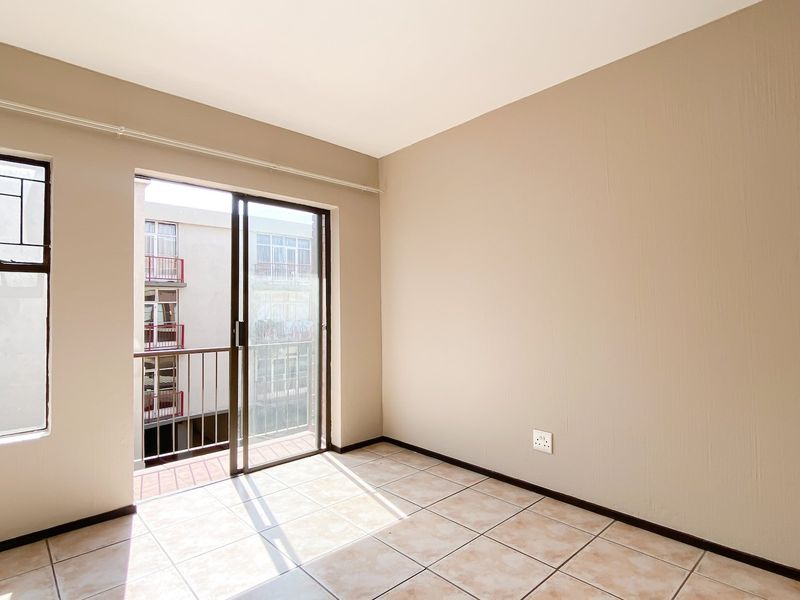 An empty bedroom featuring tiled flooring, neutral walls, and a sliding glass door providing access to a small balcony.