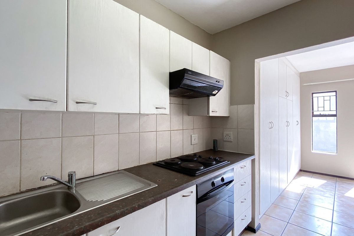 A functional kitchen featuring white built-in cabinetry, a stainless steel sink, electric hob, oven, and ample storage space with a tiled backsplash.