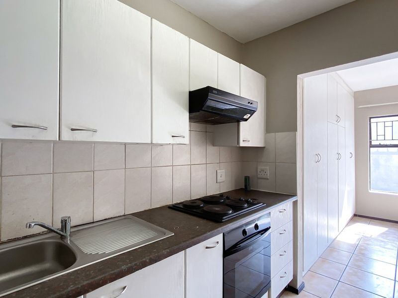 A functional kitchen featuring white built-in cabinetry, a stainless steel sink, electric hob, oven, and ample storage space with a tiled backsplash.