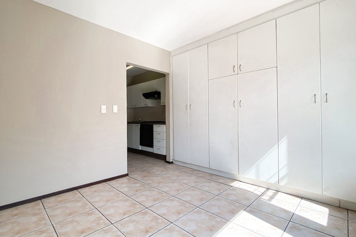 An empty living area featuring neutral tiled flooring and extensive built-in storage cupboards, with a direct view into the adjacent kitchen.