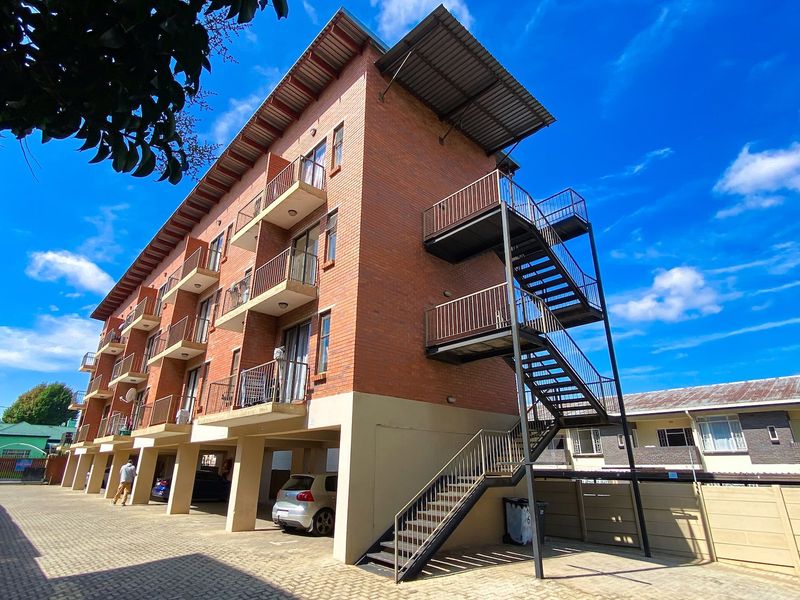 Exterior view of a multi-story apartment building featuring face brick construction, external steel staircases, private balconies, and a paved ground-level parking area.