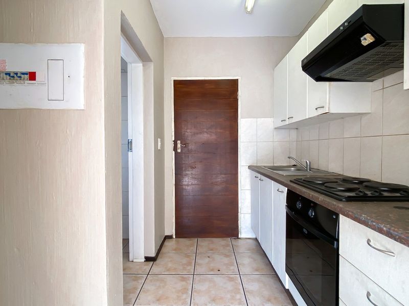 A functional kitchen featuring built-in cabinetry, a hob, an oven, an extractor fan, and tiled flooring, offering a practical layout for daily use.
