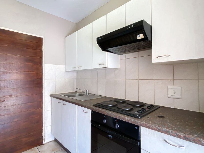 A functional kitchen featuring white cabinetry, a dark laminate countertop, built-in oven, electric hob, and extractor fan with tiled splashback.