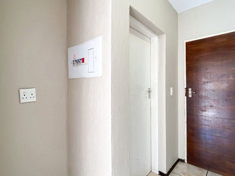 A functional hallway area featuring a wooden door, tiled flooring, and a wall-mounted electrical distribution board.