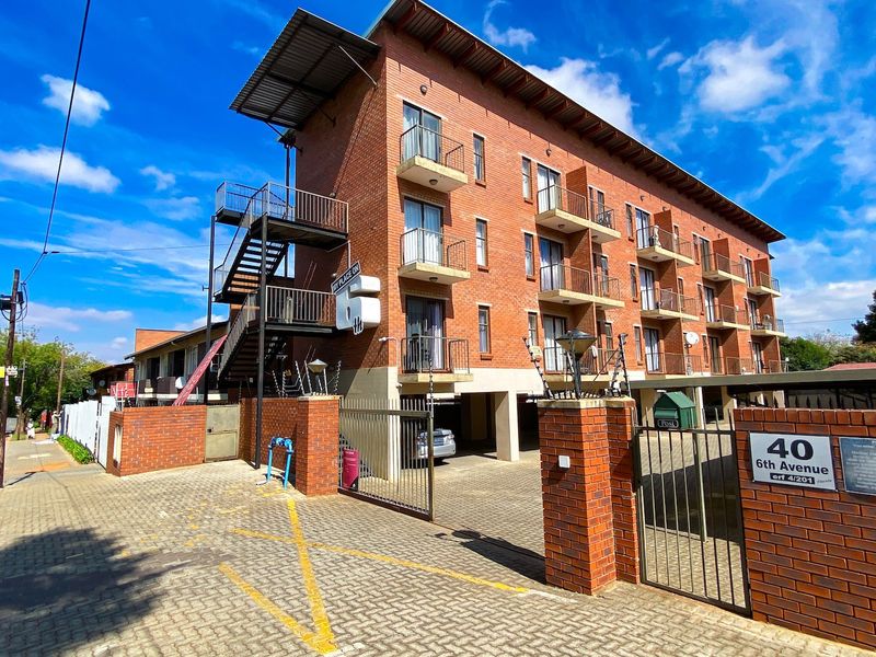 Exterior view of a multi-story brick apartment building featuring private balconies, external metal staircases, and a secure gated entrance with paved parking.