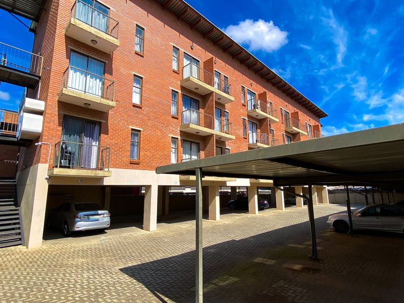 Exterior view of a multi-story brick apartment building featuring private balconies and a covered parking area with paved driveway.