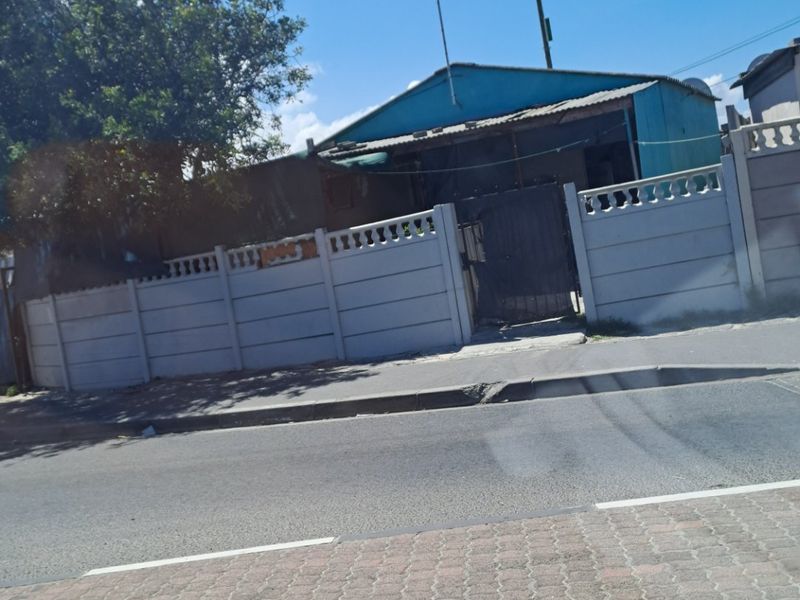 Street view of a residential property featuring a precast concrete boundary wall, metal gate, and a single-story structure with a metal roof.