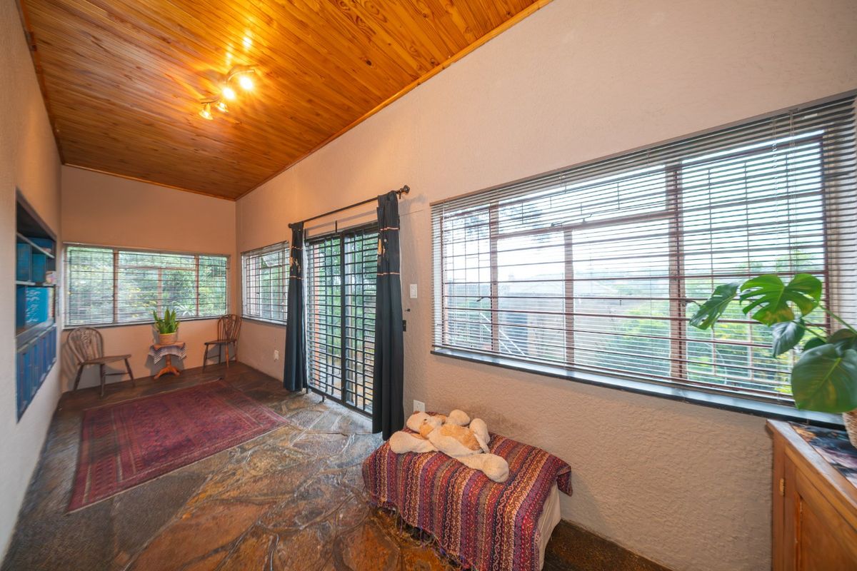 Living room featuring a warm timber ceiling, natural flagstone flooring, and large windows with venetian blinds, providing access to the exterior via a sliding door.