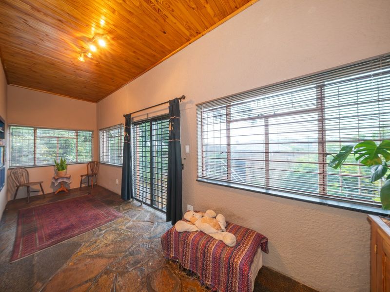 Living room featuring a warm timber ceiling, natural flagstone flooring, and large windows with venetian blinds, providing access to the exterior via a sliding door.