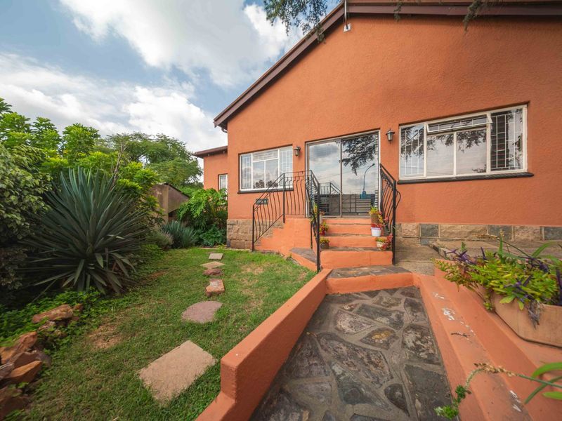Rear exterior view of the house featuring a stone-paved walkway, steps with wrought iron railings, and sliding glass door access to the garden.
