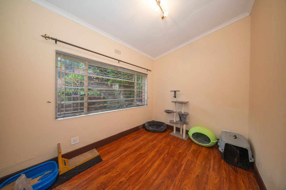 A vacant bedroom featuring laminate flooring, a large window with security bars, and venetian blinds, offering a blank canvas for personalization.