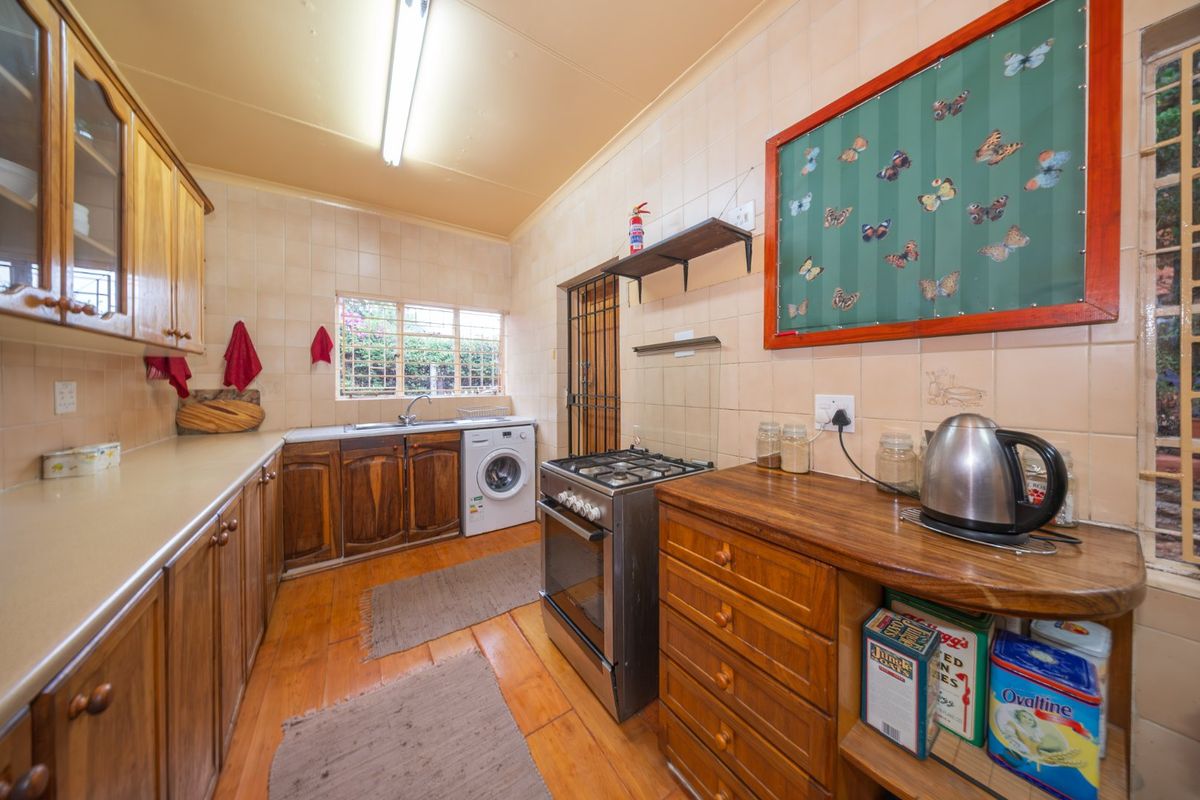 A functional kitchen featuring wooden cabinetry, laminate countertops, a freestanding gas stove, and integrated laundry plumbing, offering a classic, dated aesthetic.