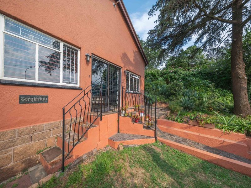 Rear exterior view of the house featuring a sliding door entrance, stone masonry base, and wrought iron railings leading to a landscaped garden area.