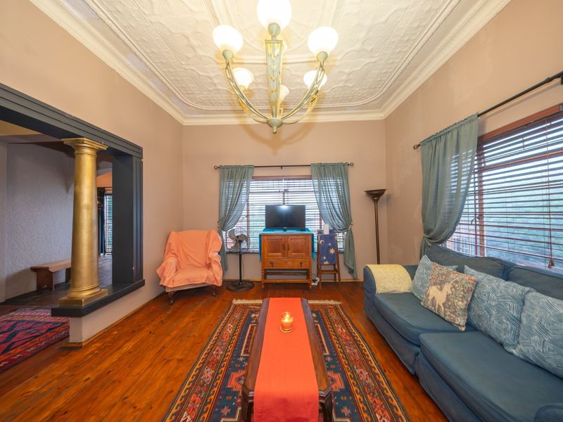 A living room featuring original pressed metal ceilings, hardwood flooring, and a decorative column, offering a classic architectural character with potential for cosmetic updates.