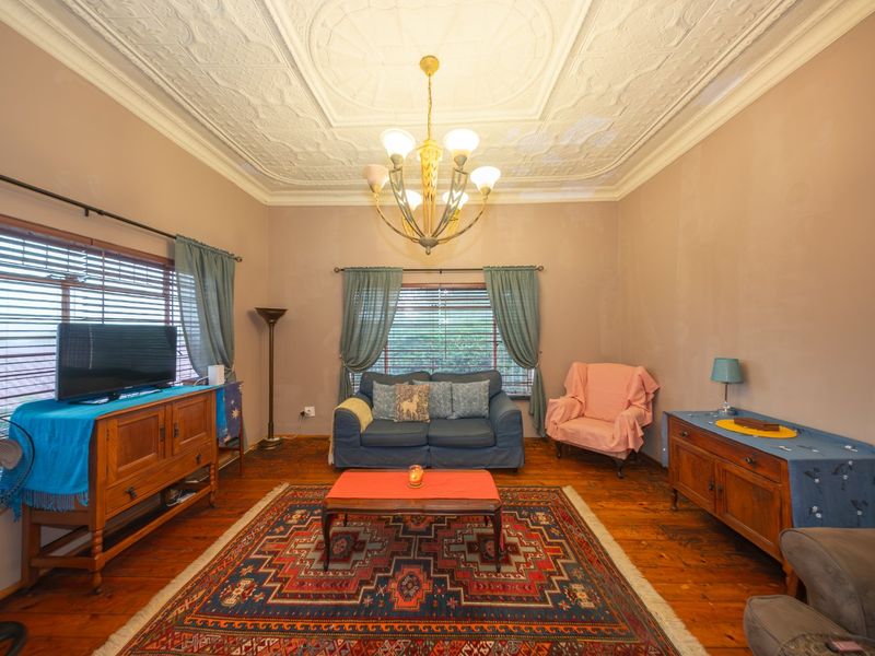 A living room featuring original timber flooring and an ornate pressed metal ceiling, showing signs of wear and water damage on the ceiling and walls.