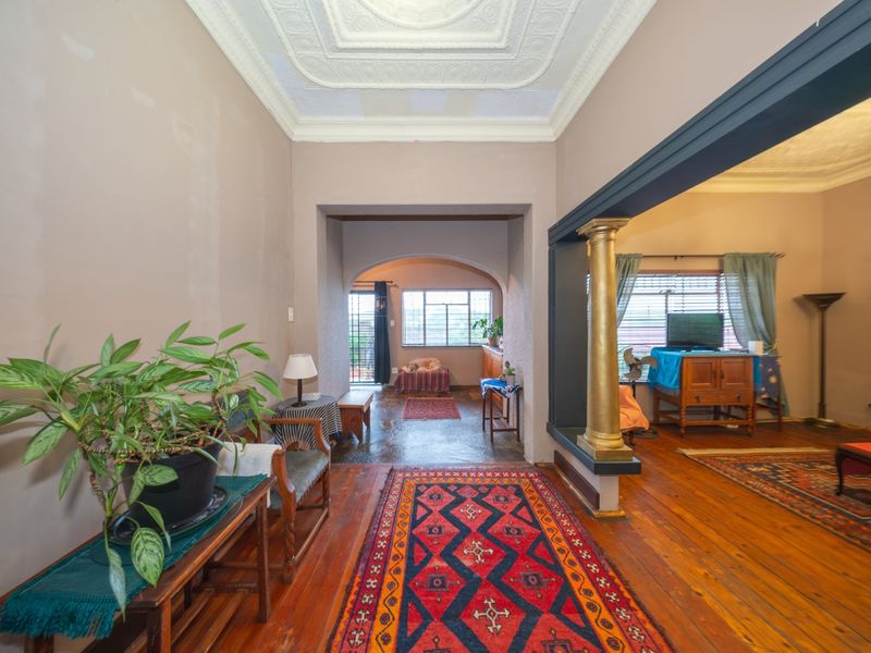 Spacious living area featuring original hardwood flooring, ornate ceiling detailing, and a decorative column, offering a classic architectural foundation for modern updates.