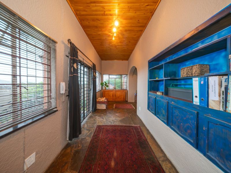 A spacious hallway featuring a warm timber ceiling, stone flooring, and built-in blue cabinetry, providing access to adjacent living areas.