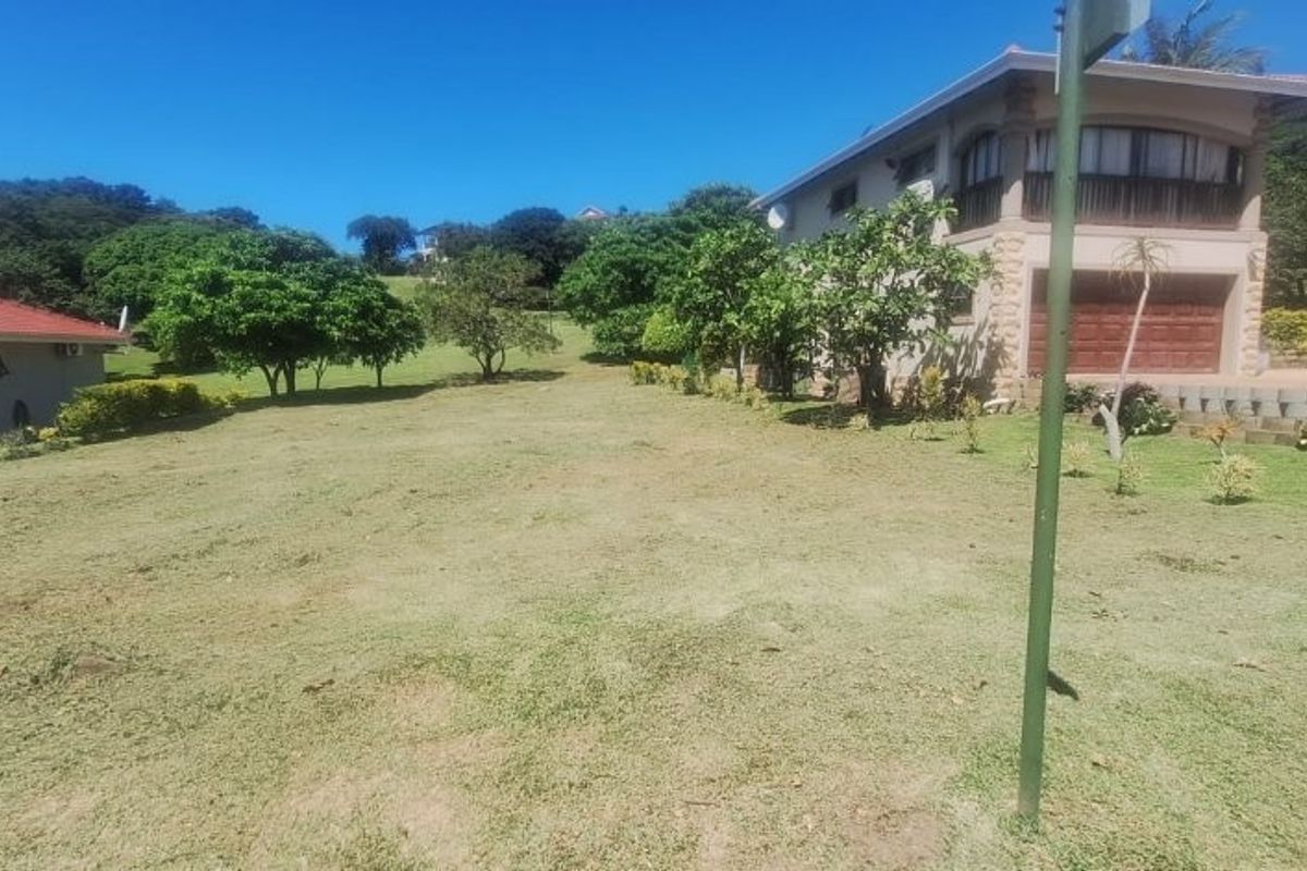 A spacious, well-maintained residential garden area featuring mature trees and a gentle slope, adjacent to existing property structures.