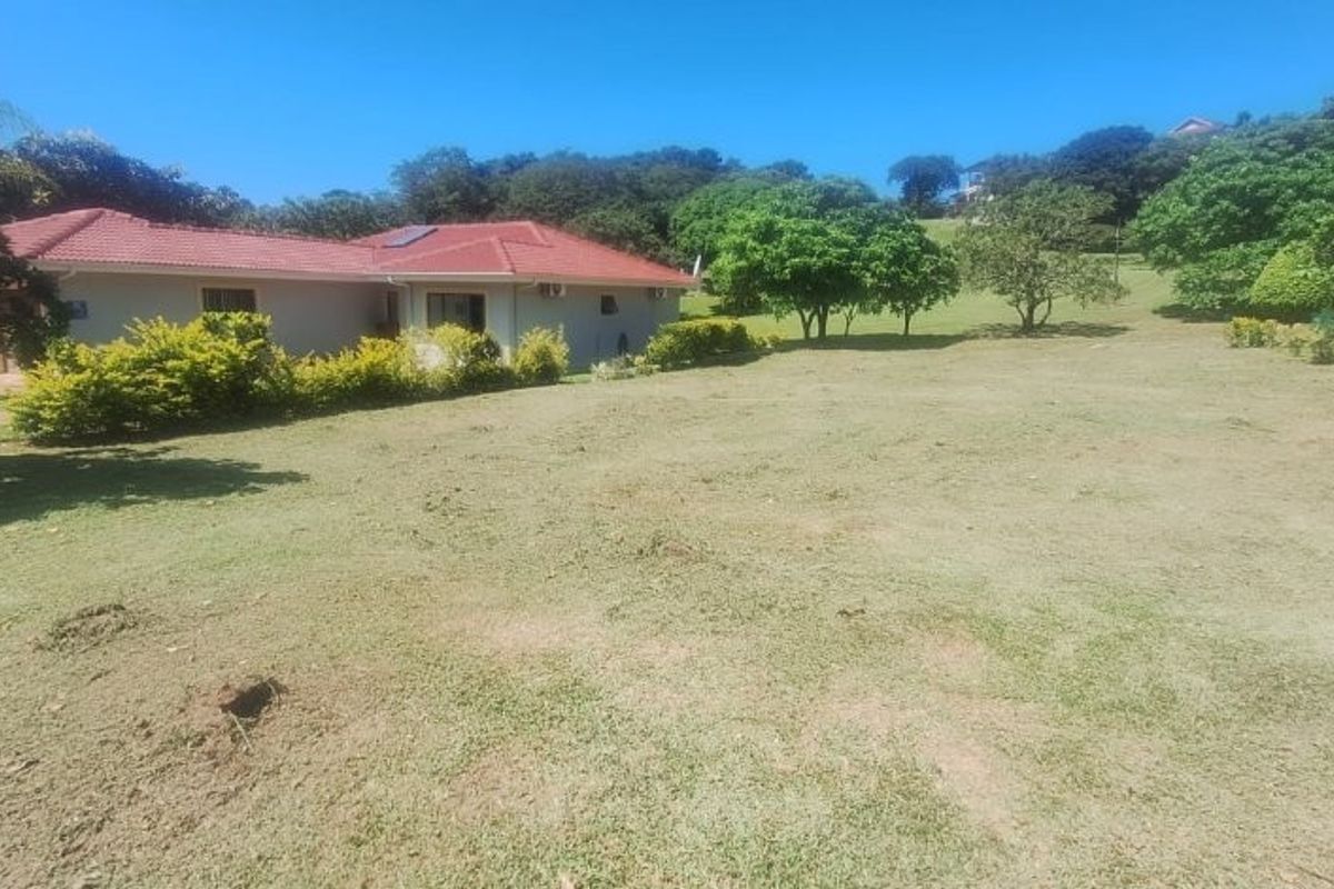 A spacious, well-maintained residential garden featuring a large lawn, mature trees, and established hedging, adjacent to a single-story dwelling.