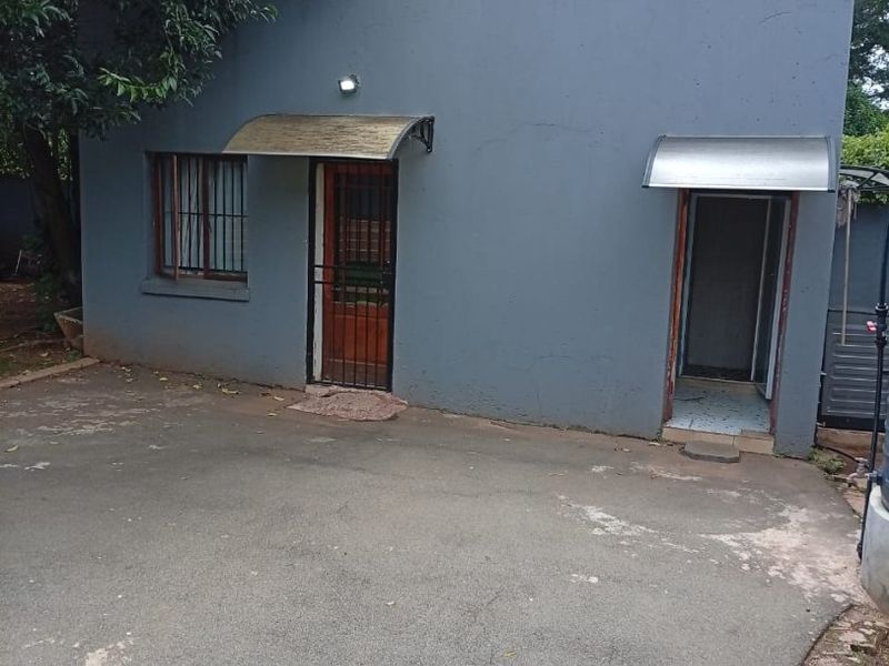Rear exterior view of the property featuring a grey rendered facade, security gates, and protective awnings over the entrances.