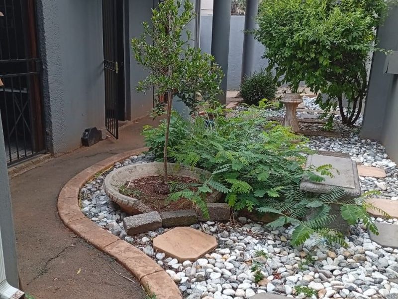 A covered patio area featuring concrete columns, a paved walkway, and a landscaped garden bed with pebble accents.