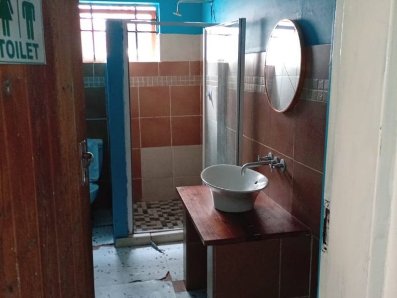 A dated bathroom featuring a vessel sink on a wooden vanity, a separate shower enclosure, and a toilet, requiring cosmetic updates and repairs.